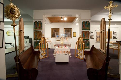 Visible in this photo are the six icons of the Apostles, which are displayed in the icon wall of this exhibit. Also, the icons that appear in the “Deacon’s doors” in this exhibit are from this older icon wall - although the doors have since been re-built as part of a new icon wall. The processional fan and cross that mounted on the end of the pews inside the church date from the earliest years of the parish. These pews are also from the Holy Ghost Ukrainian Catholic church. They have been refinished in honor of the parish’s centenary.

The stained glass windows in the exhibit are from the original Holy Ghost Ukrainian Catholic Church, built in 1913.