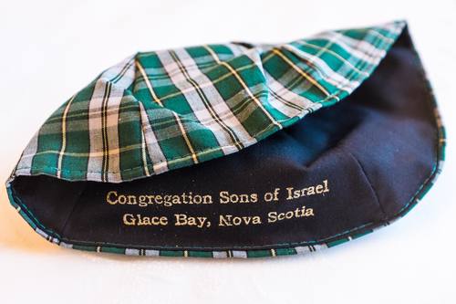 A photo of a ceremonial kippah head covering worn by Jews during prayer. This kippah features the tartan pattern common to Cape Breton, with the name of the synagogue printed inside.