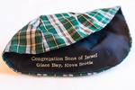 A photo of a ceremonial kippah head covering worn by Jews during prayer. This kippah features the tartan pattern common to Cape Breton, with the name of the synagogue printed inside.