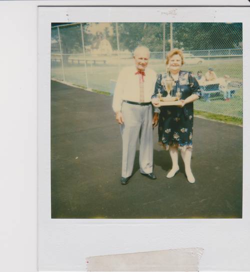 Photograph of couple with trophy in woman's arms. Man wearing embroidered shirt. 