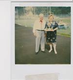 Photograph of couple with trophy in woman's arms. Man wearing embroidered shirt. 