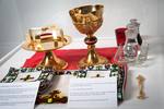 The Proskomediynyk, or Table of Preparation

Sitting on a red cloth are the Chalice, Paten and Star. They are used to transfer the bread and wine from the Proskomediynyk to the Prystil, or Altar - and used to distribute Holy Communion.

In the foreground are three Chalice covers, embroidered to match the priest’s vestments – one cover for the Paten, one for the Chalice, and the Great Cover to cover both.

To the right of the Chalice covers is the Spear, used during the prayers to prepare the bread for Holy Communion.

Above the Spear are two cruets containing water and fortified red wine, used for Holy Communion.

Two candles illuminate the table.

The tablecloths on the Table of Needs, Altar and Table of Preparation were all embroidered by parishioner Tekla Mulak in 1985.
